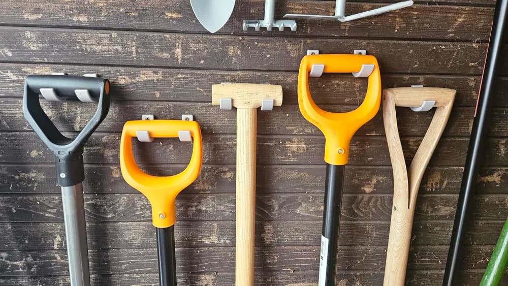 Grey 3D printed wall clips holding garden tool handles on a wooden wall